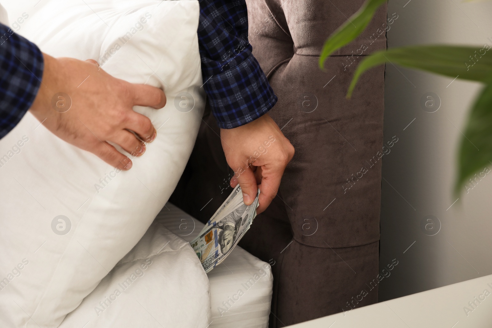 Photo of Man hiding dollar banknotes under pillow in bedroom, closeup. Money savings