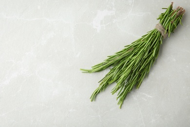 Photo of Bundle of fresh rosemary on light grey marble background, top view. Space for text