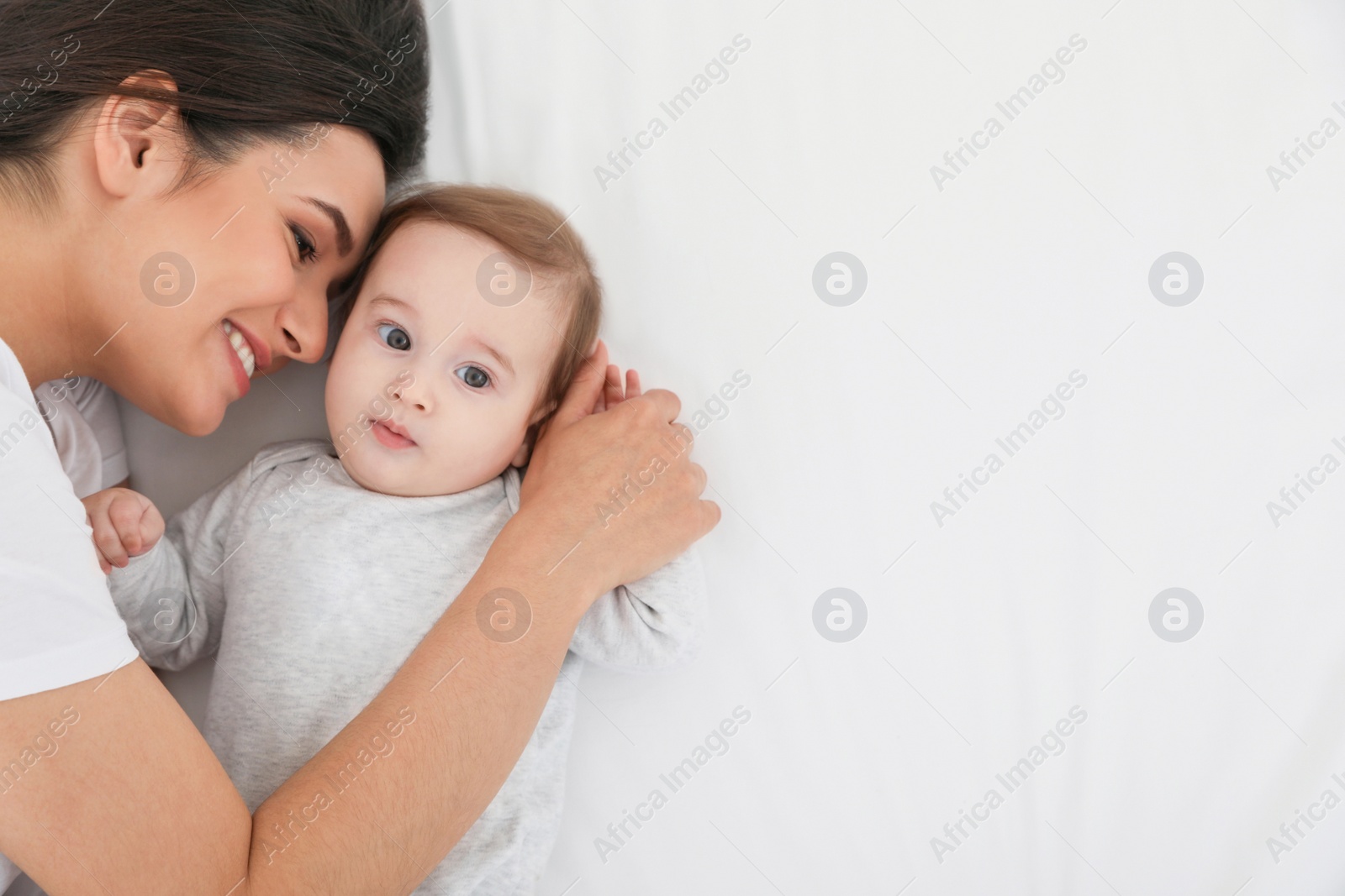 Photo of Portrait of mother with her cute baby lying on bed, top view. Space for text