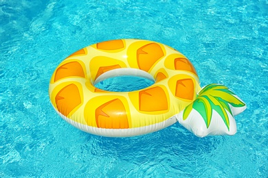 Photo of Bright inflatable pineapple ring floating in swimming pool on sunny day