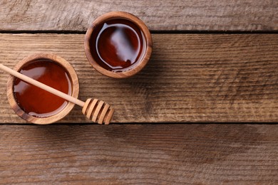 Photo of Delicious honey in bowls and dipper on wooden table, flat lay. Space for text