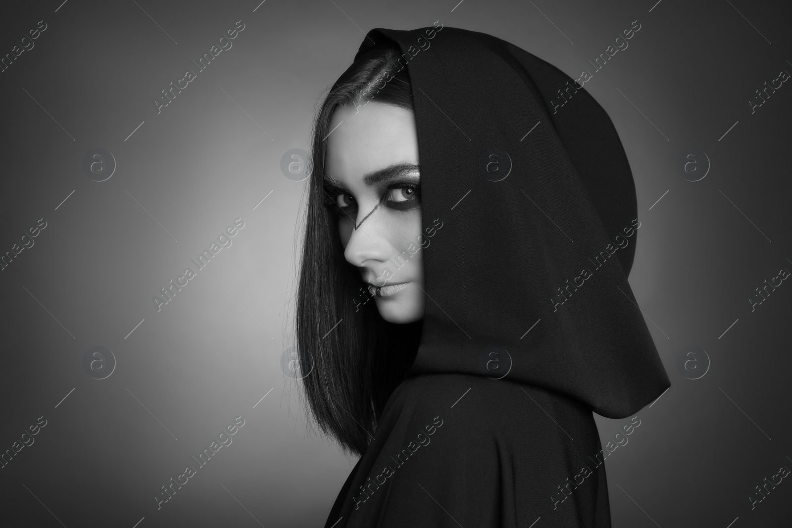 Photo of Mysterious witch in mantle with hood on dark background. Black and white effect