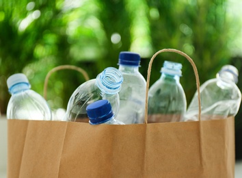 Photo of Paper bag with used plastic bottles against blurred background, closeup. Recycle concept