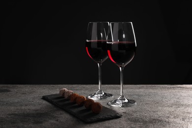 Photo of Red wine and chocolate truffles on gray table against dark background, space for text