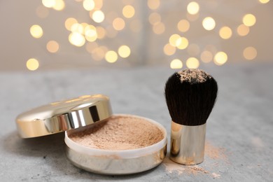 Photo of Face powder and brush on grey textured table against blurred lights, closeup