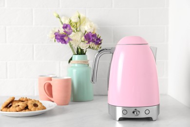 Photo of Modern electric kettle, bouquet, cookies and cups on counter in kitchen