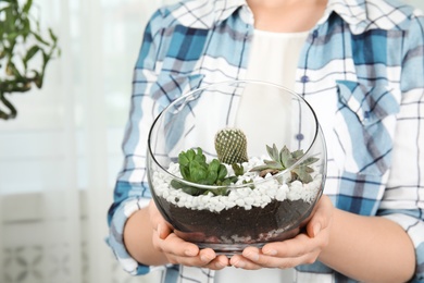 Young woman holding florarium with different succulents indoors, closeup