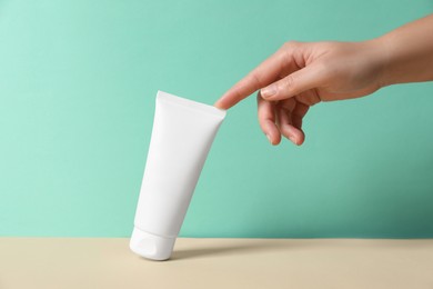 Photo of Tube of hand cream on beige table against turquoise background, closeup