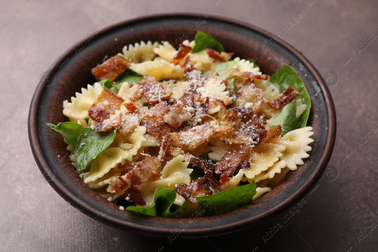 Photo of Tasty pasta with bacon and basil on brown table, closeup