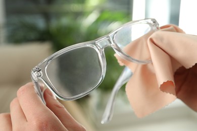 Photo of Woman cleaning glasses with microfiber cloth at home, closeup