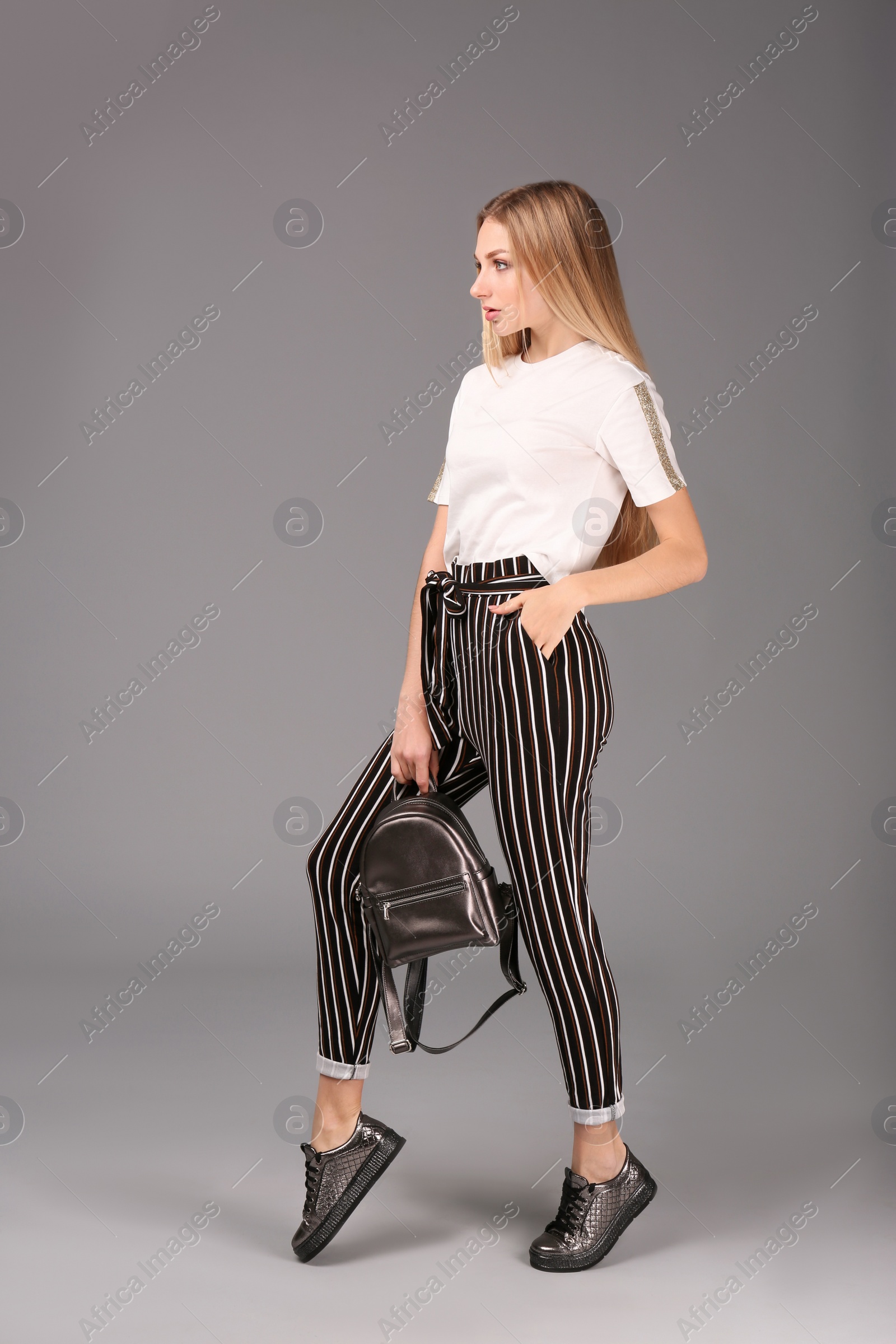 Photo of Young stylish woman in trendy sport shoes with backpack on grey background