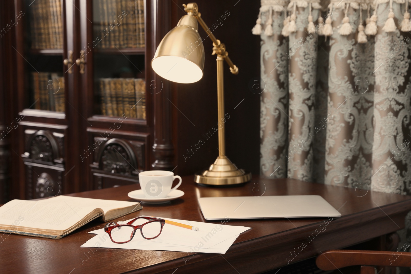 Photo of Laptop, book and papers on wooden table in library reading room