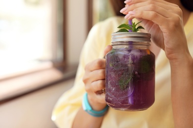 Young woman with mason jar of tasty natural lemonade in cafe, closeup. Detox drink