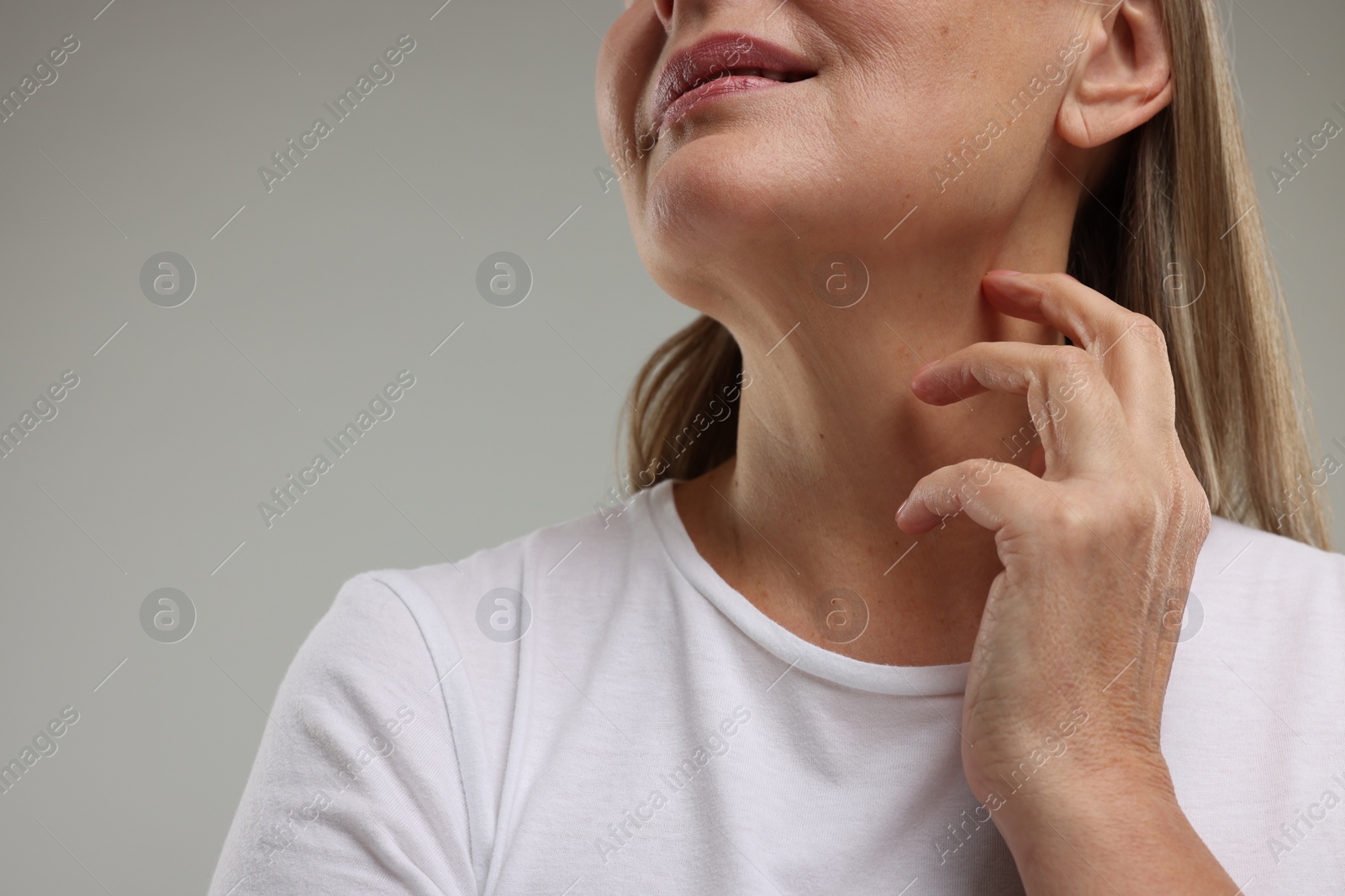 Photo of Mature woman touching her neck on grey background, low angle view