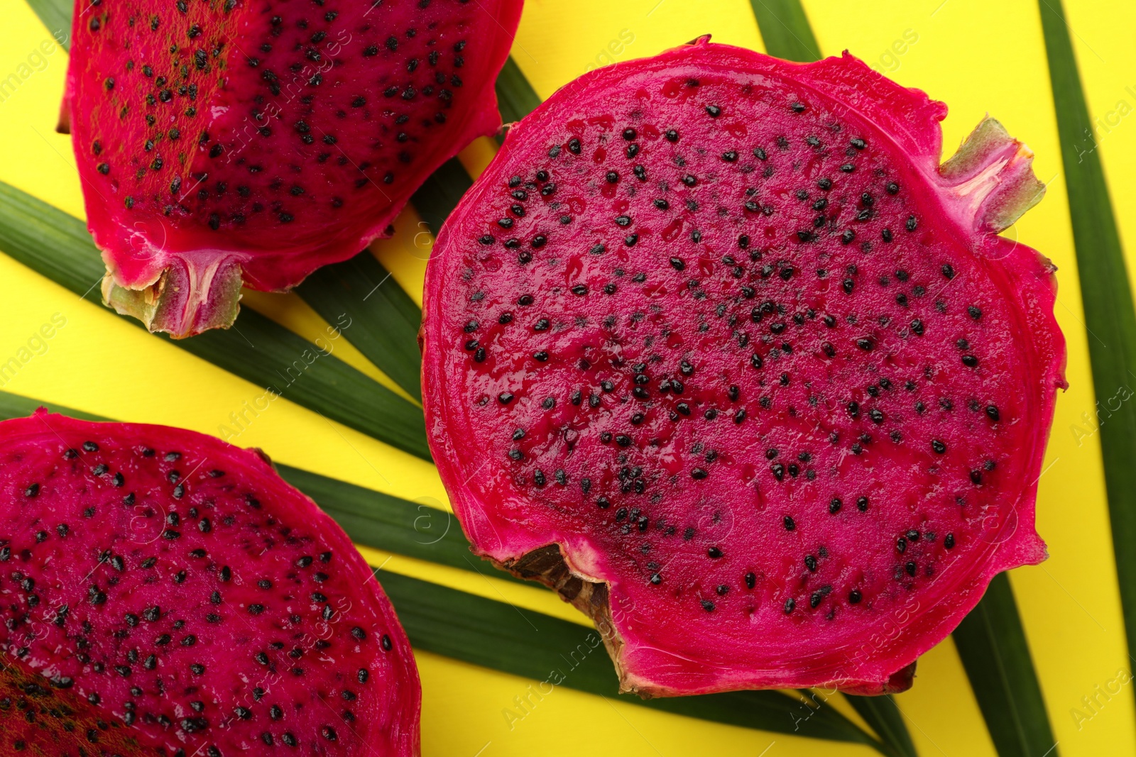 Photo of Delicious cut red pitahaya fruit with palm leaf on yellow background, flat lay