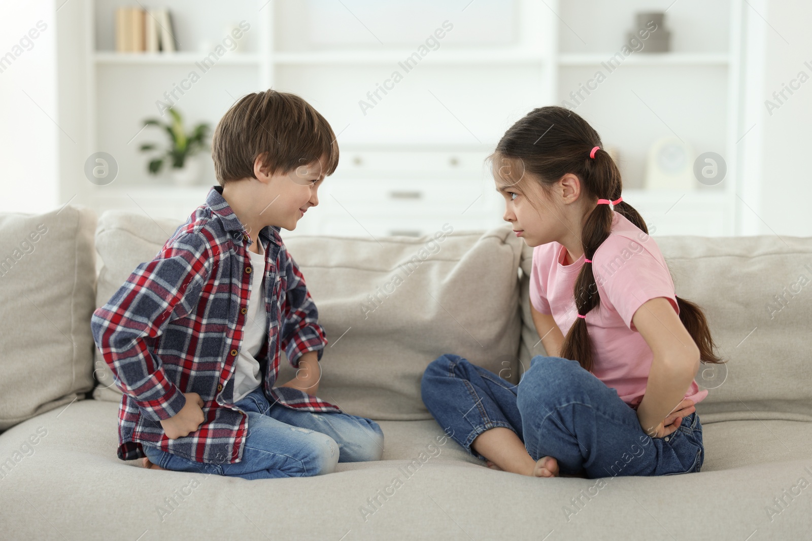 Photo of Upset brother and sister having argument on sofa at home