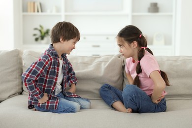 Photo of Upset brother and sister having argument on sofa at home