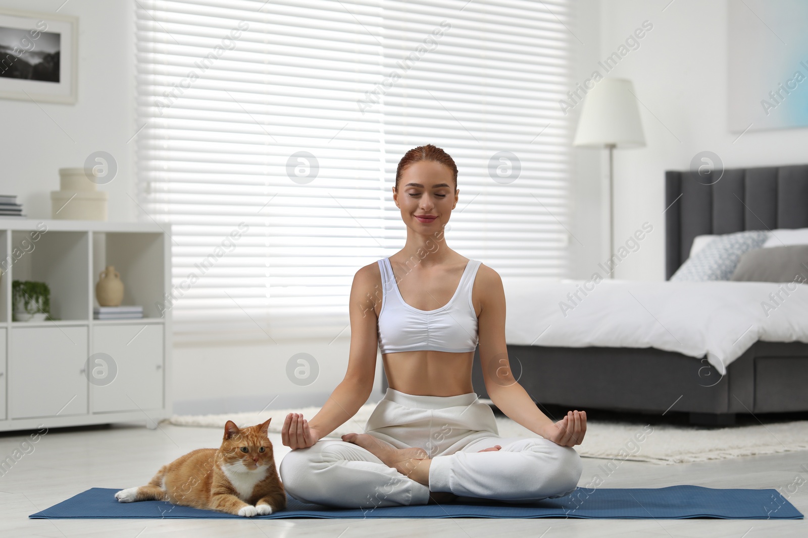 Photo of Beautiful woman with cute red cat practicing yoga on mat at home