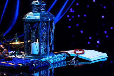 Photo of Arabic lantern, Quran, misbaha, Aladdin magic lamp, dates and folded prayer mat on mirror surface against blurred lights at night. Space for text