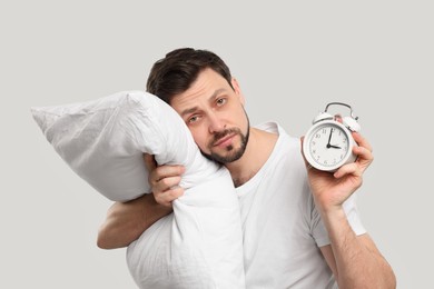 Tired man with alarm clock and pillow on light grey background. Insomnia problem