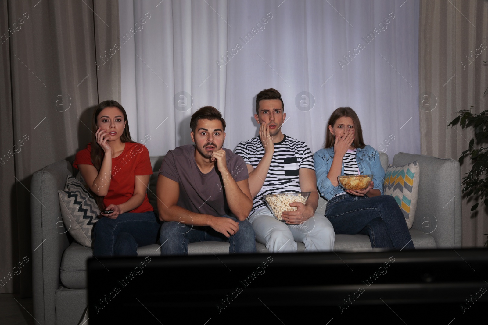 Photo of Group of people with snacks watching TV together on couch in dark room