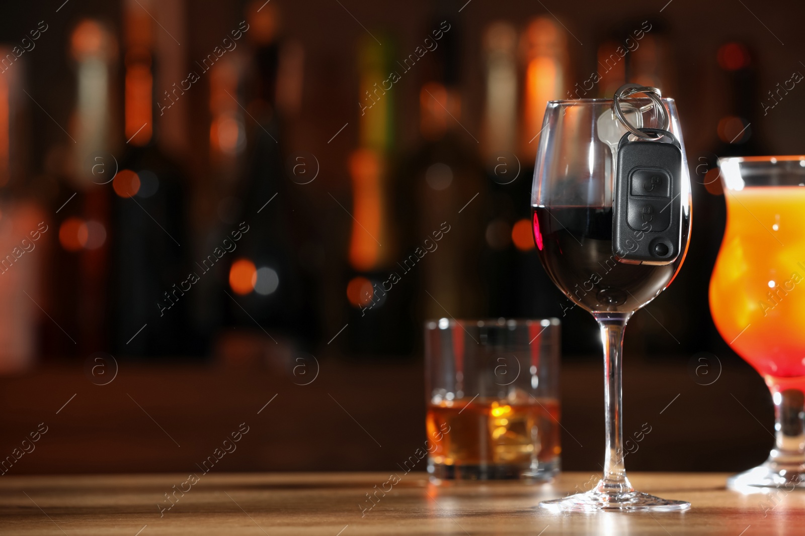 Photo of Car key and glass of alcoholic drink on table against blurred background, space for text. Drunk driving concept