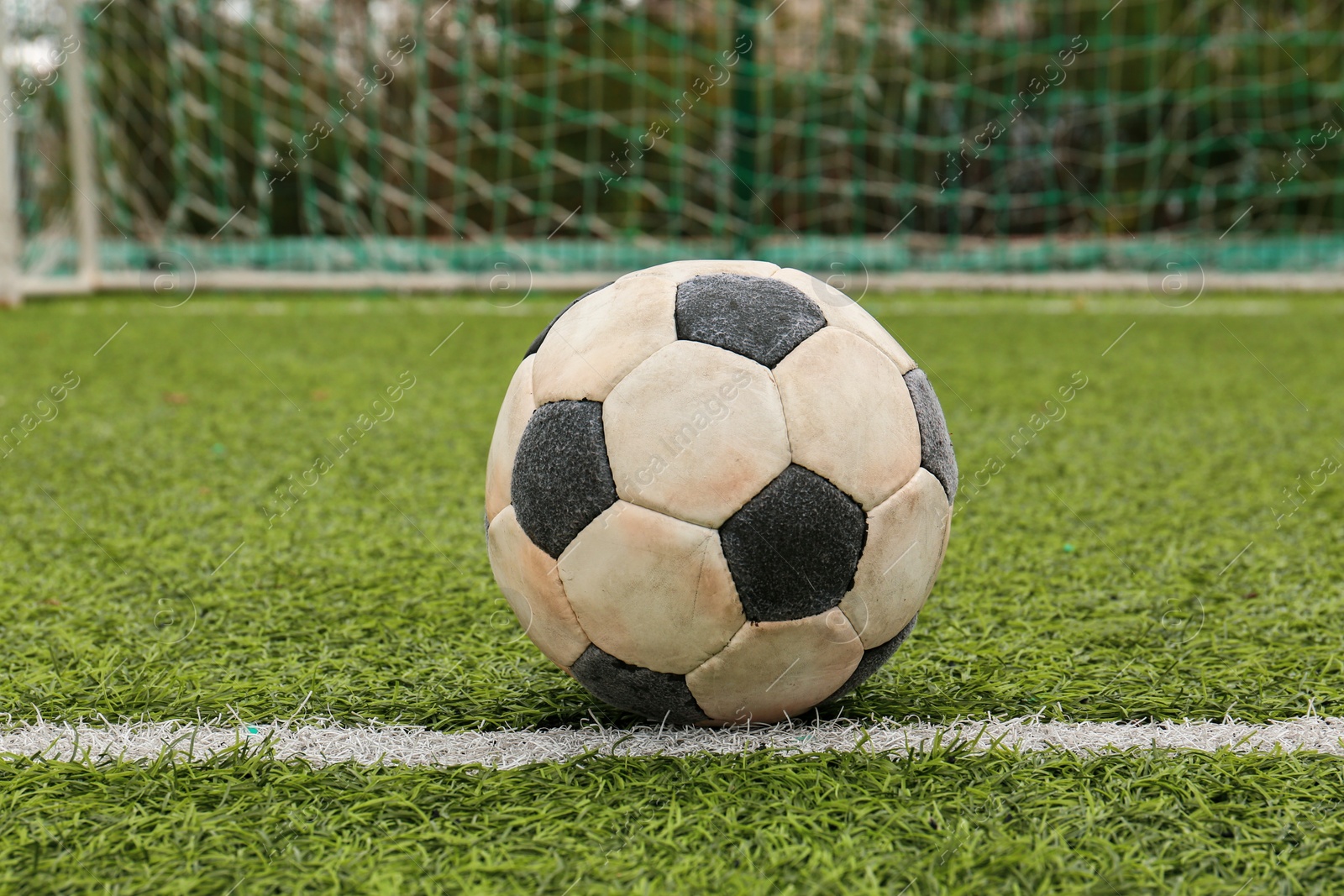 Photo of Dirty soccer ball on green football field against net