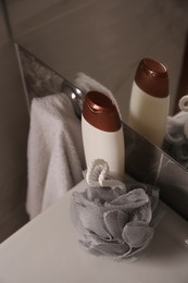 Grey sponge and shower gel bottle on washbasin in bathroom