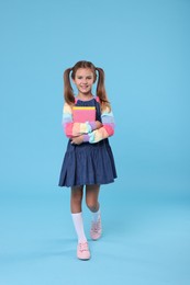 Photo of Happy schoolgirl with books on light blue background