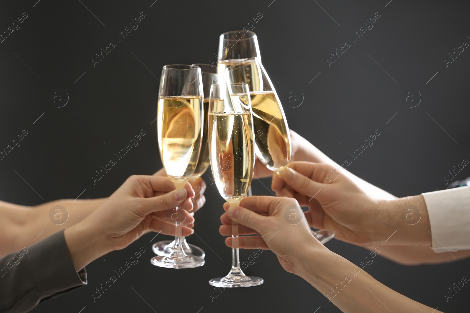 Photo of People clinking glasses of champagne on dark background, closeup