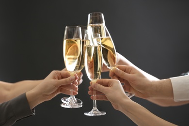 Photo of People clinking glasses of champagne on dark background, closeup