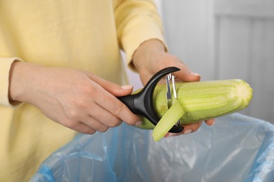 Photo of Woman peeling fresh zucchini above garbage bin indoors, closeup