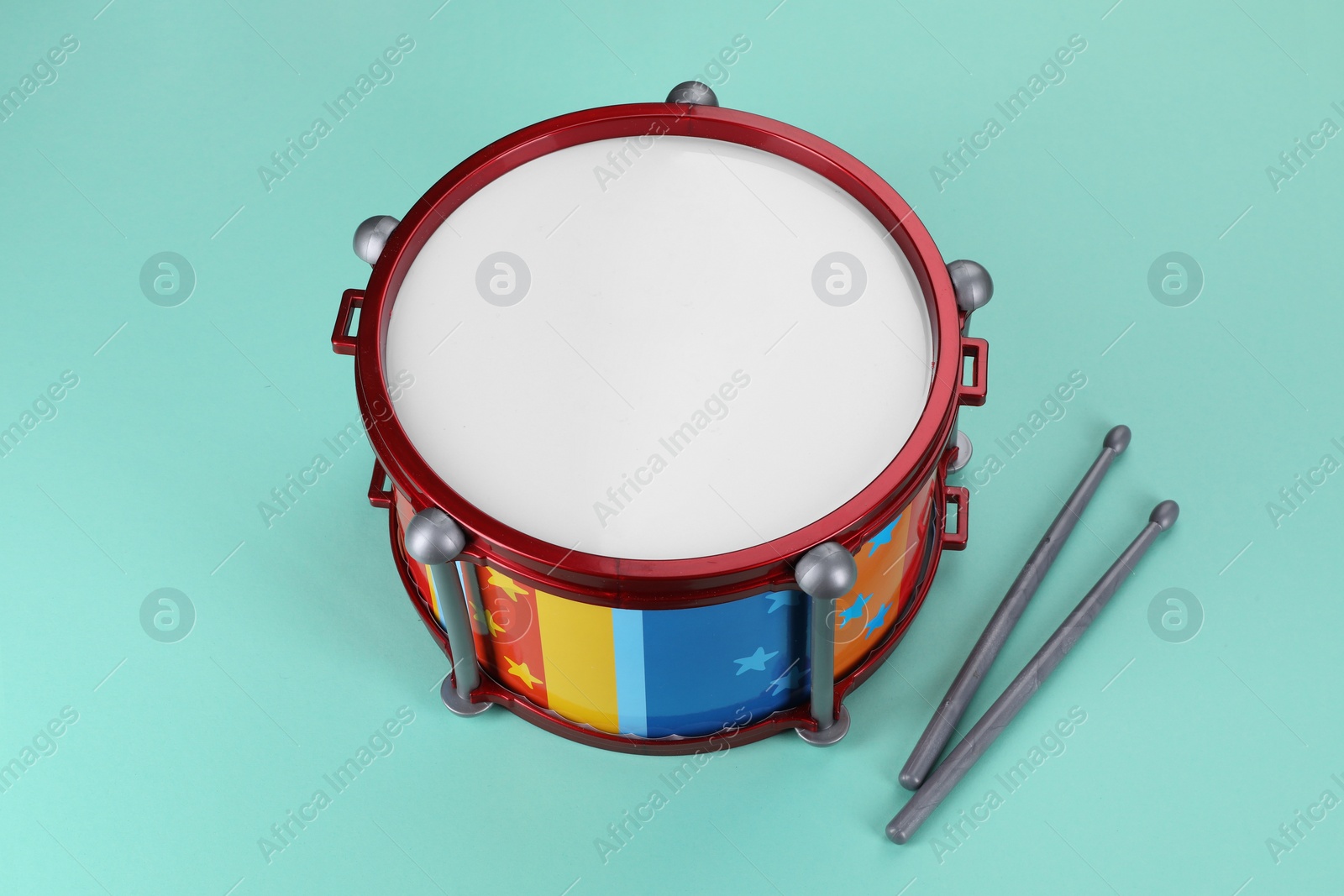 Photo of Children's drum with drumsticks on turquoise background