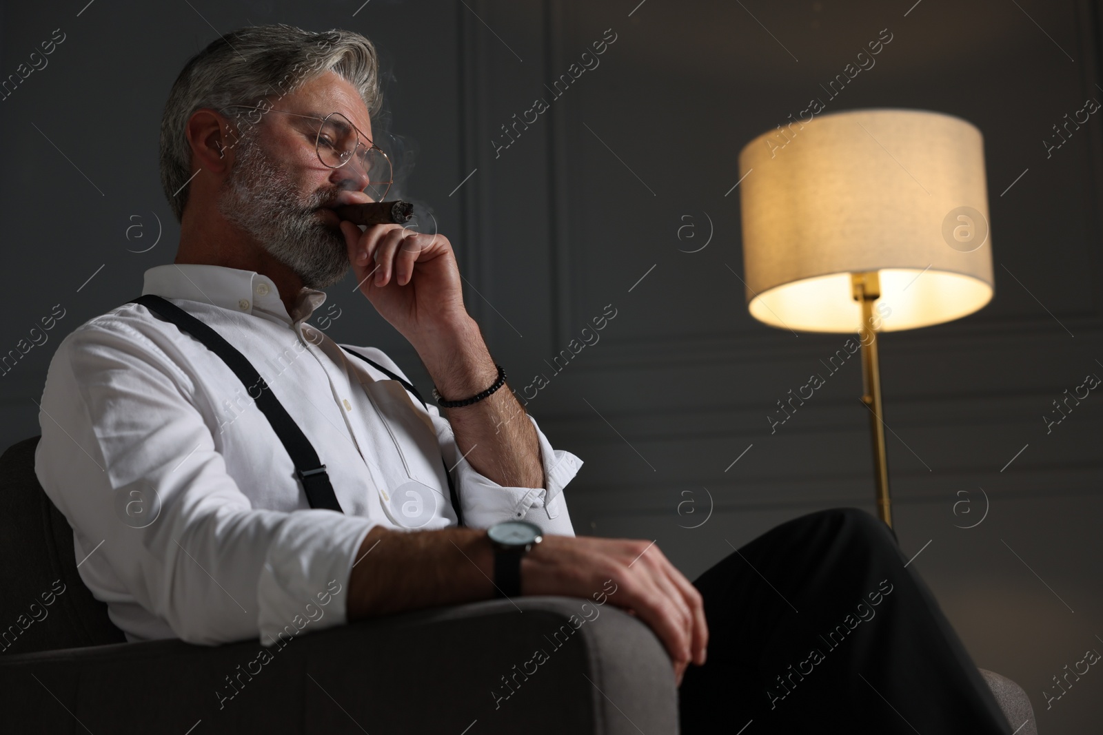 Photo of Bearded man smoking cigar in armchair indoors. Space for text