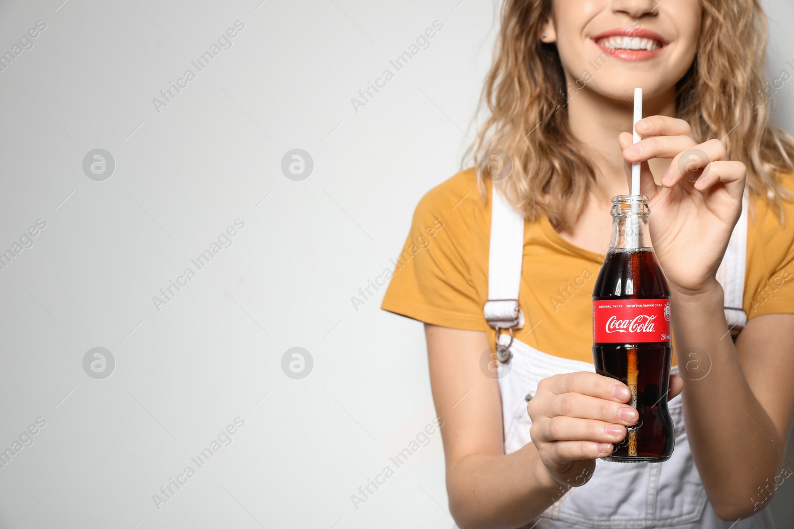 Photo of MYKOLAIV, UKRAINE - NOVEMBER 28, 2018: Young woman with bottle of Coca-Cola on white background, closeup. Space for text