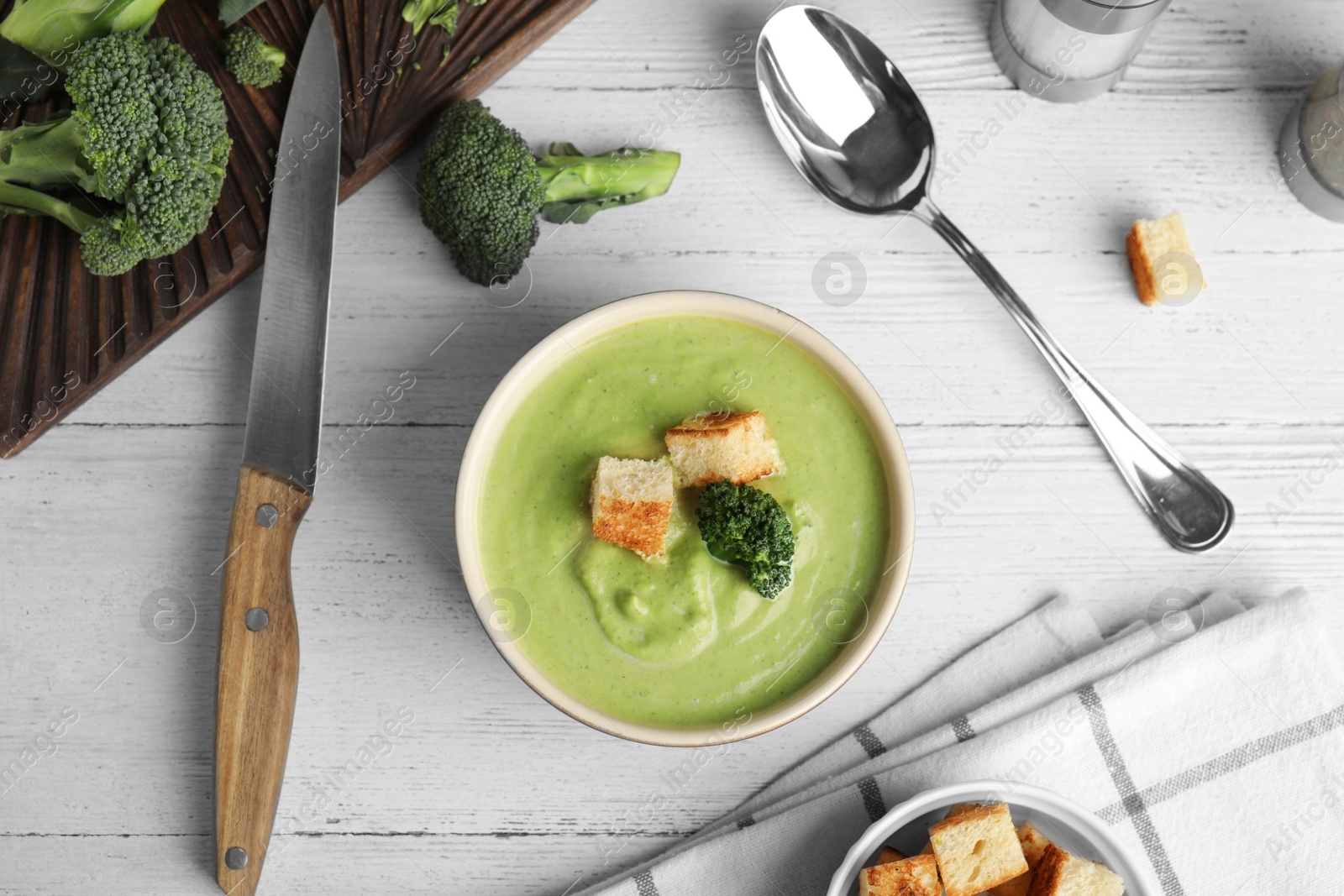 Photo of Delicious broccoli cream soup with croutons served on white wooden table, flat lay