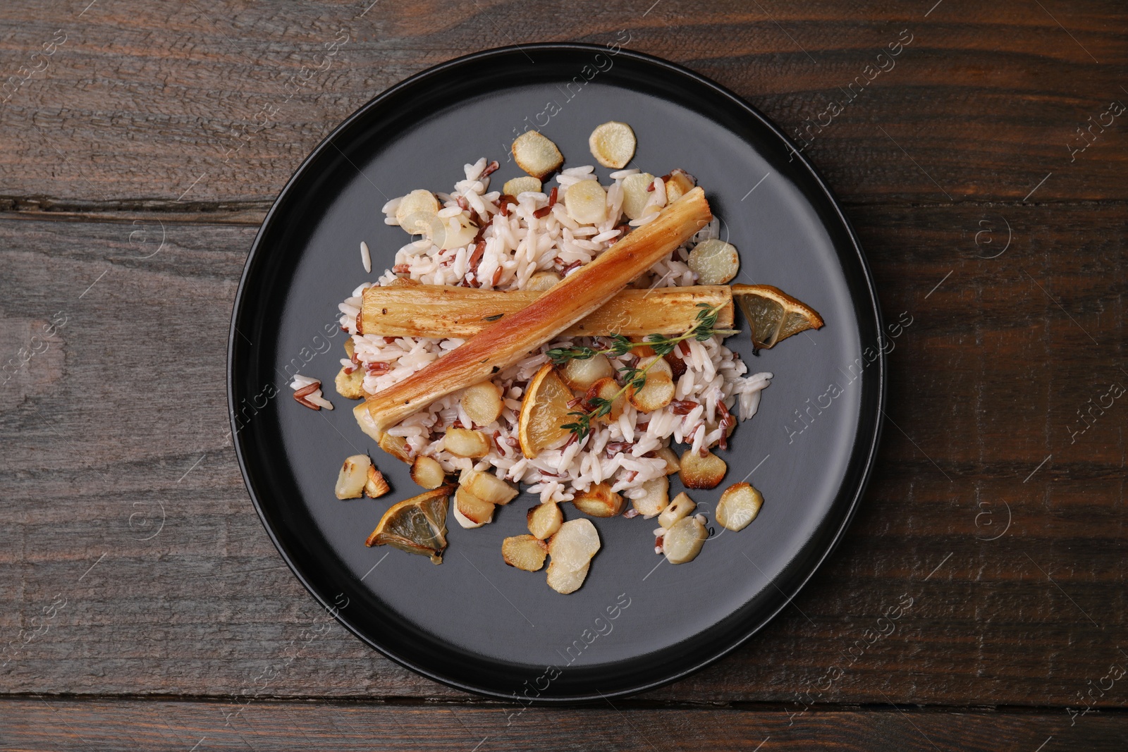 Photo of Plate with baked salsify roots, lemon and rice on wooden table, top view