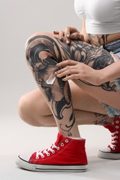 Woman applying healing cream onto her tattoos against light background, closeup
