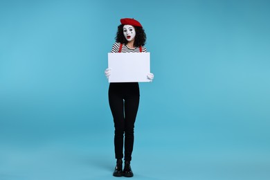 Funny mime with blank sign posing on light blue background