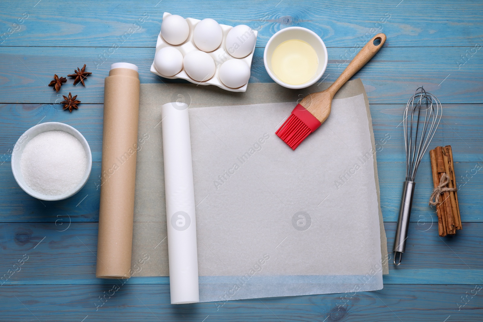 Photo of Rolls of baking parchment paper, different ingredients and kitchen tools on light blue wooden table, flat lay. Space for text