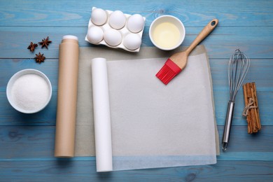 Photo of Rolls of baking parchment paper, different ingredients and kitchen tools on light blue wooden table, flat lay. Space for text