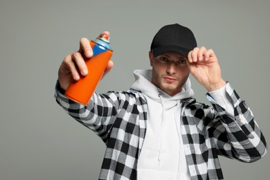 Handsome man holding used can of spray paint on grey background