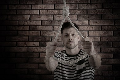 Image of Depressed man with rope noose near brick wall. Suicide concept