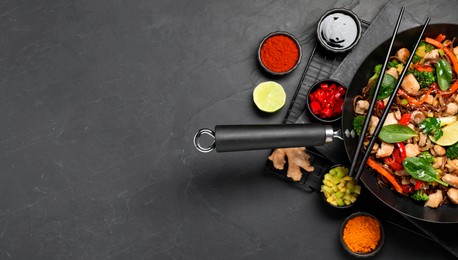 Photo of Stir-fry. Tasty noodles with meat in wok, chopsticks and ingredients on grey textured table, flat lay. Space for text