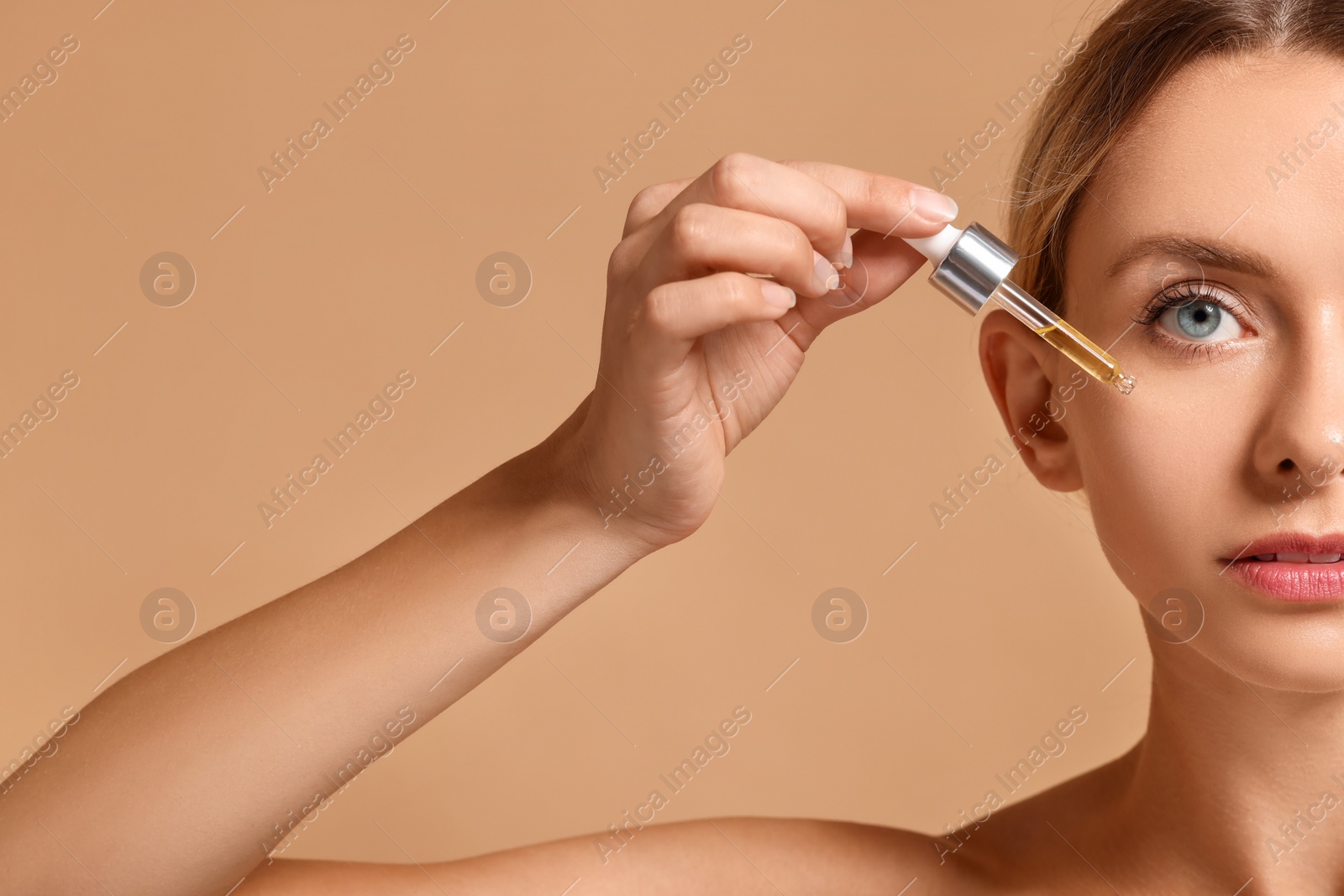 Photo of Woman applying cosmetic serum onto her face on beige background, closeup