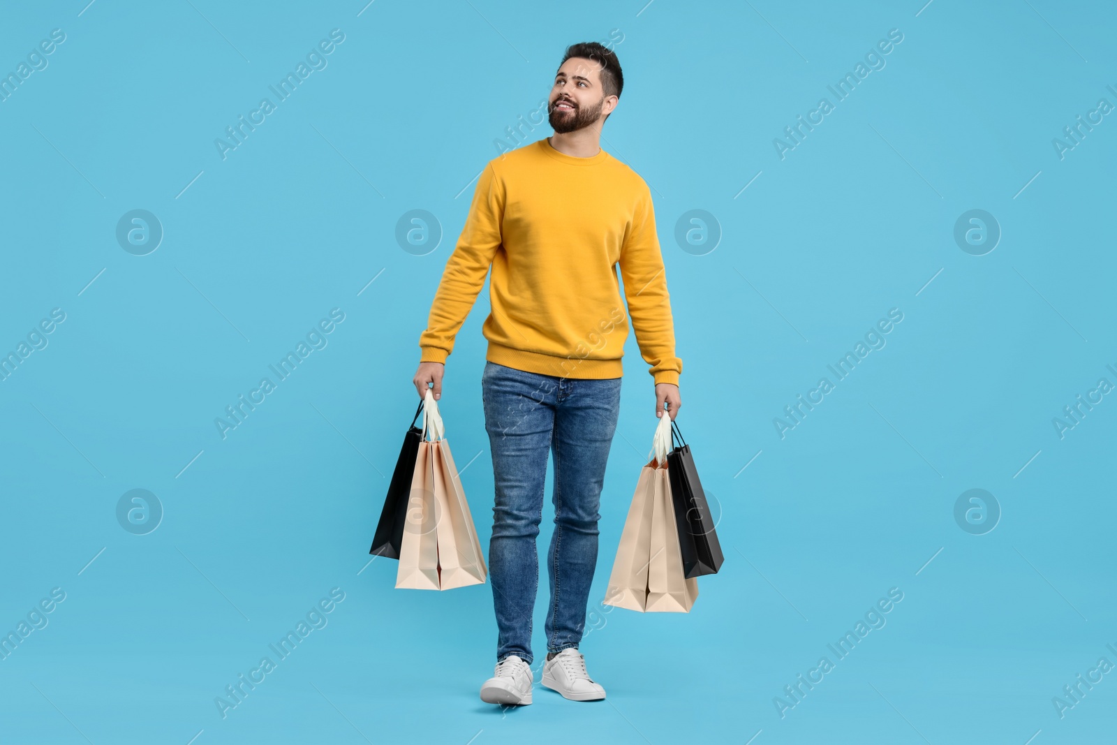 Photo of Happy man with many paper shopping bags on light blue background