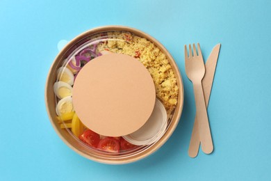 Photo of Tasty food in container with wooden fork and knife on light blue background, flat lay. Space for text