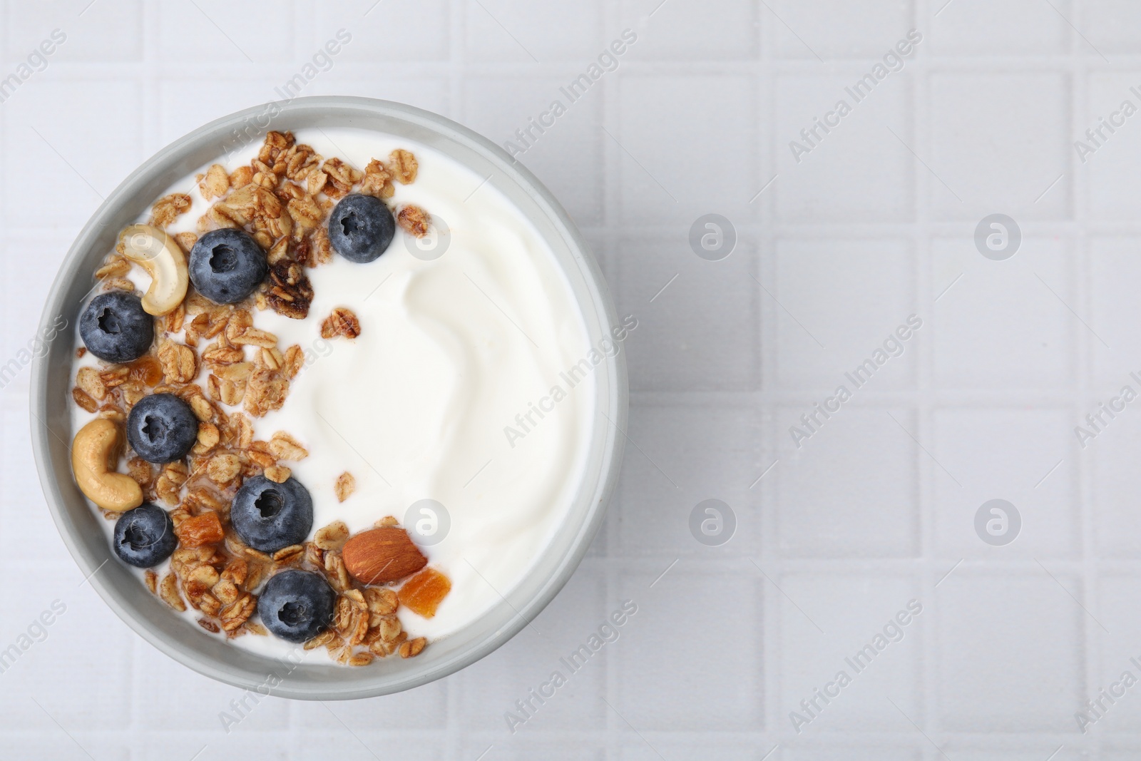 Photo of Bowl with yogurt, blueberries and granola on white tiled table, top view. Space for text