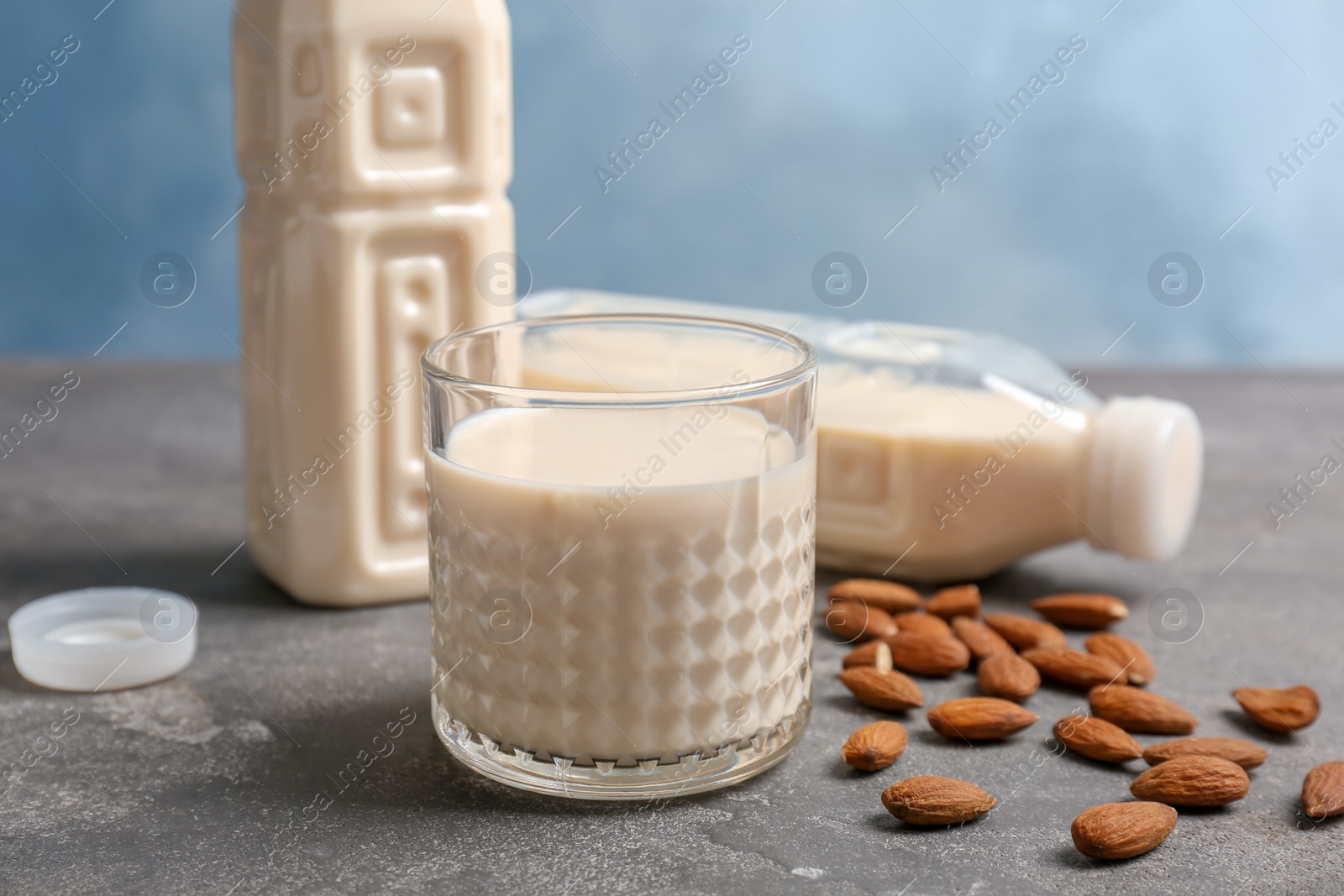 Photo of Glass and bottles with almond milk on grey table