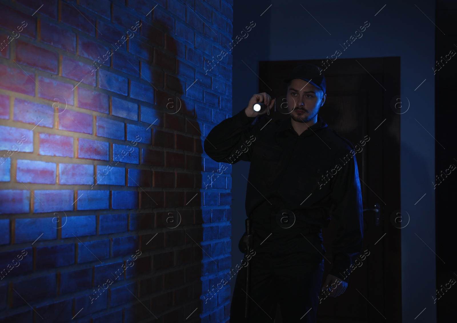 Photo of Male security guard with flashlight in dark corridor